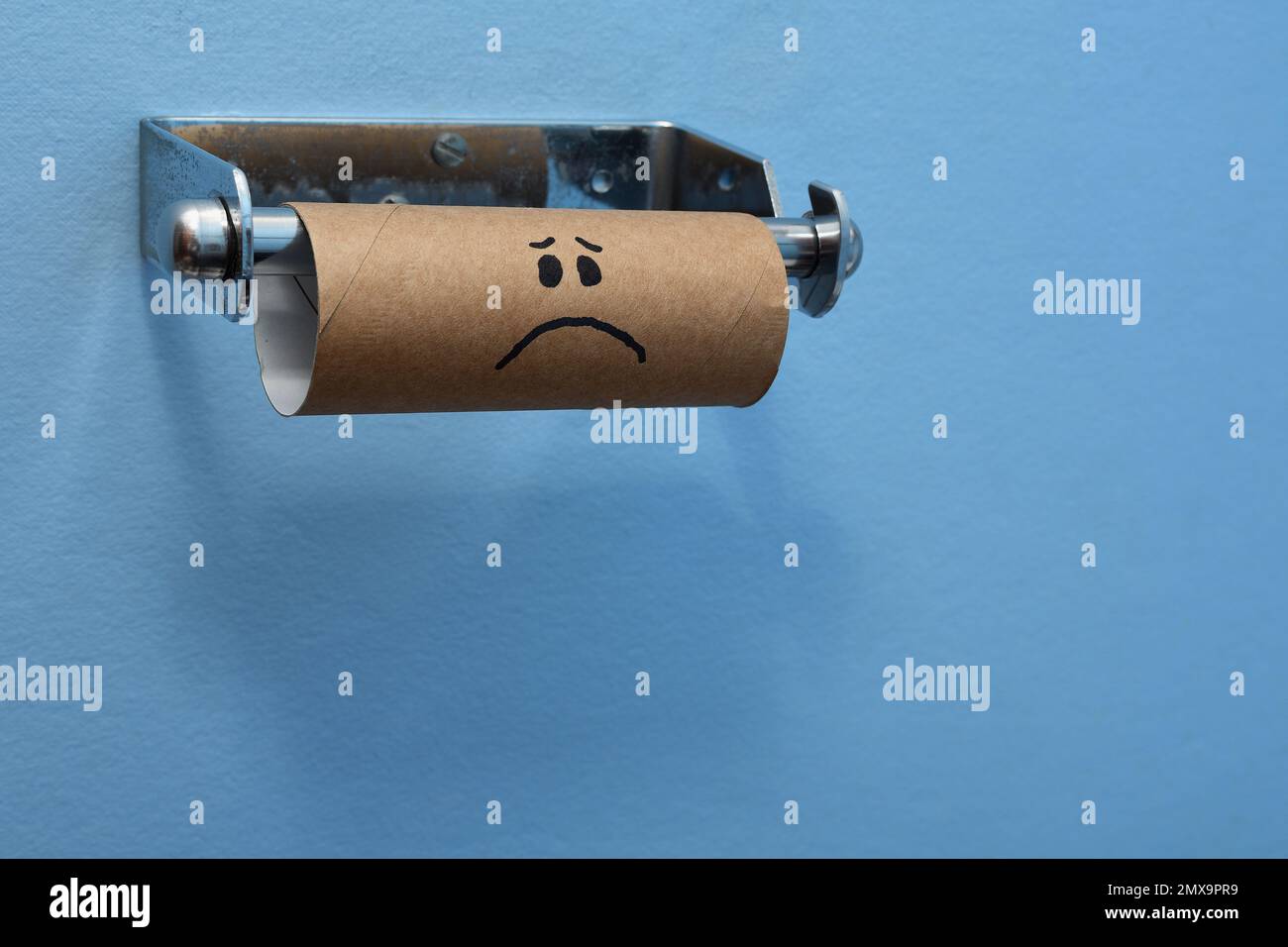 Einer traurigen braunen Toilettenpapierrolle aus Pappe ist das Toilettenpapier/Taschentücher ausgegangen, auf einem hellblauen Hintergrund links vom Rahmen Stockfoto