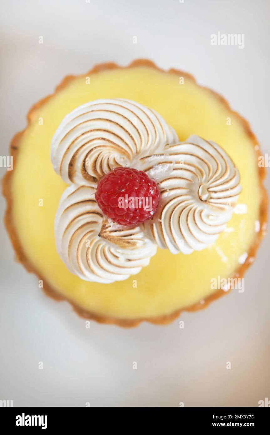 Blick hinunter auf eine köstliche Zitronentorte mit Meringue und einer frischen roten Himbeere auf einem weißen Tisch. Stockfoto