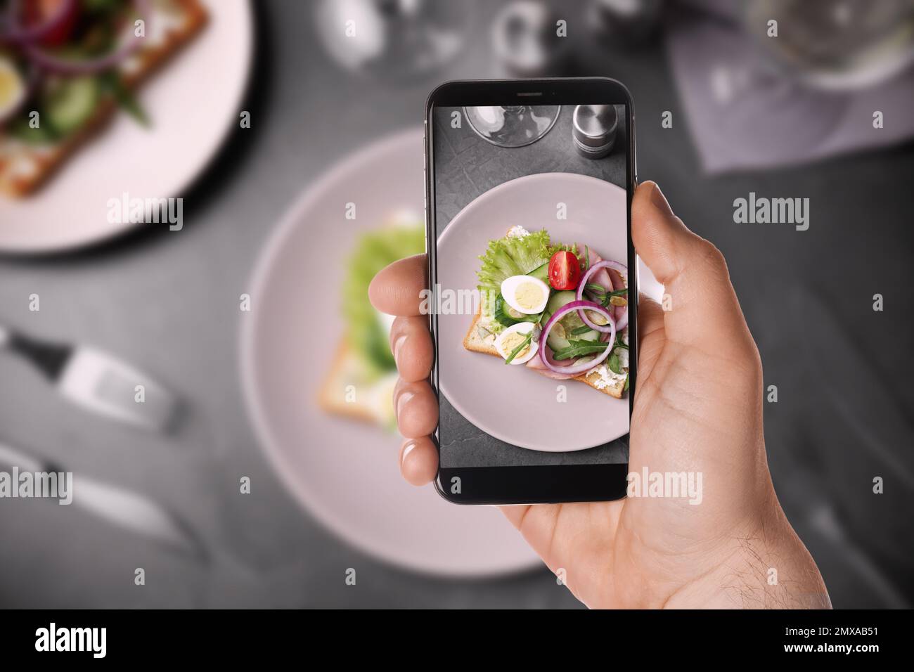 Blogger macht ein Foto von einem köstlichen Sandwich mit Schinken am Tisch, Nahaufnahme. Lebensmittelfotografie Stockfoto