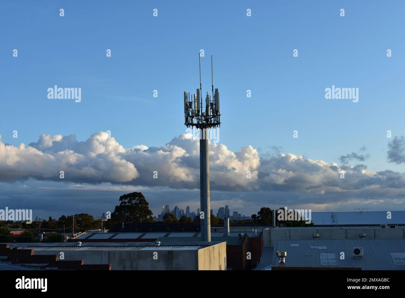 5G Mobilfunkmast vor einem blauen Himmel mit einer Stadt in der Ferne. Stockfoto