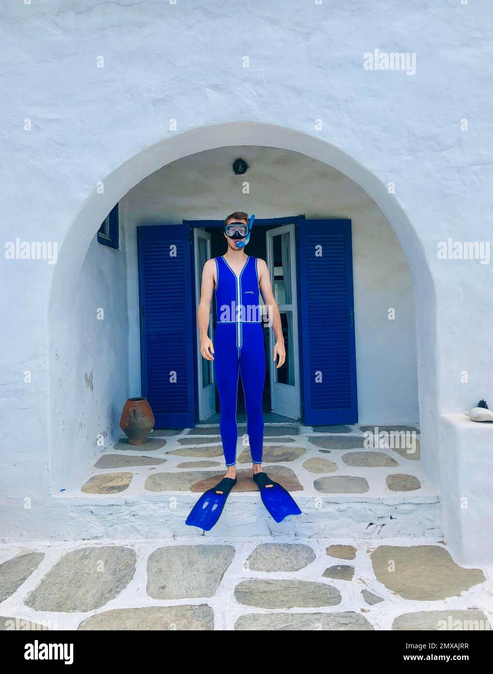 Junger Mann in blauem Neoprenanzug mit Flossen, Taucherbrille und Schnorchel, steht vor dem weißen Kykladen Haus, Paros, Kykladen Inseln, Griechenland Stockfoto