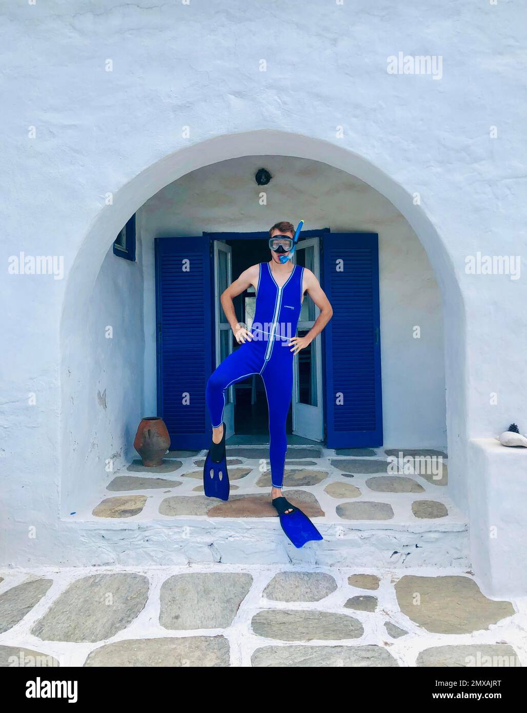 Junger Mann in blauem Neoprenanzug mit Flossen, Schutzbrille und Schnorchel, posiert vor dem weißen Kykladen-Haus, Paros, Kykladen-Inseln, Griechenland Stockfoto
