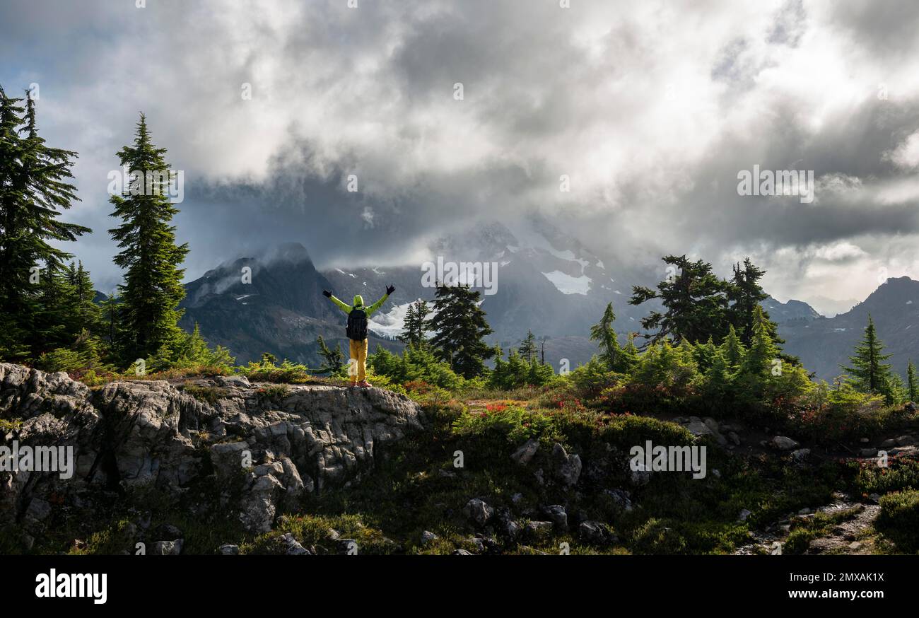 Wanderer streckt seine Arme in der Luft vor dem bewölkten Mt. Shuksan mit Schnee und Gletscher, dramatisch bewölkter Himmel, Mt. Baker-Snoqualmie National Forest Stockfoto