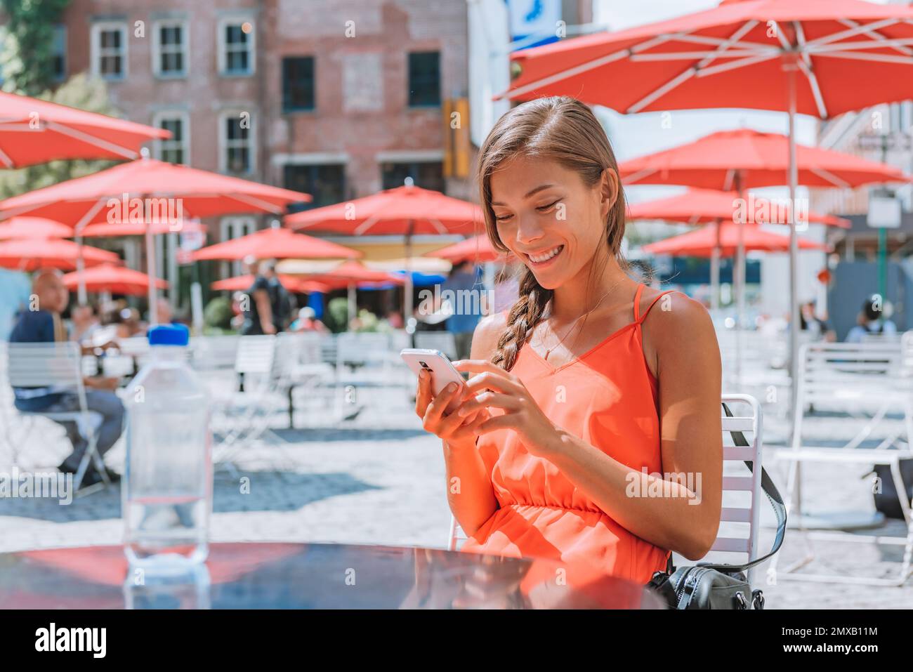 Eine Frau, die telefonisches Trinkwasser benutzt, sitzt an einem Tisch in der New Yorker City Street in Gansevoort Plaza, einem öffentlichen Ort im Meatpacking District von New York City. Mädchen Stockfoto