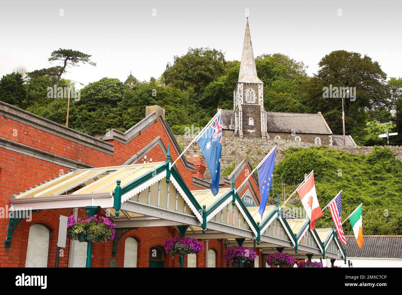 Kreuzfahrtanleger aus rotem Backstein und Heritage Center, dekoriert mit Flaggen der Welt und Cobh-Museum, das sich in der Schottischen Kirche, Cobh, in der Nähe von Cork, Irland befindet Stockfoto