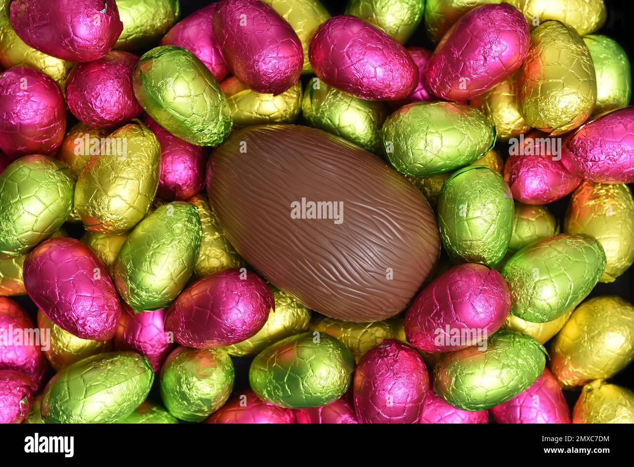 Ein Stapel mehrfarbiger und in verschiedenen Größen verpackter Schokoladeneier in Pink, Rot, Gelb und Limettengrün mit einem Ei. Stockfoto