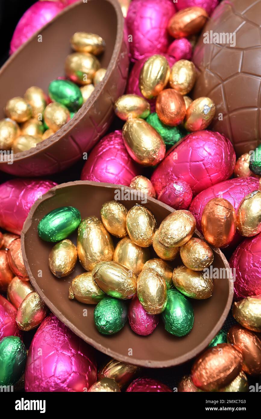 Ein Stapel bunter und in verschiedenen Größen mit bunten Folien verpackter Schokoladeneier in Pink, Rot, Gold und Limettengrün. Stockfoto