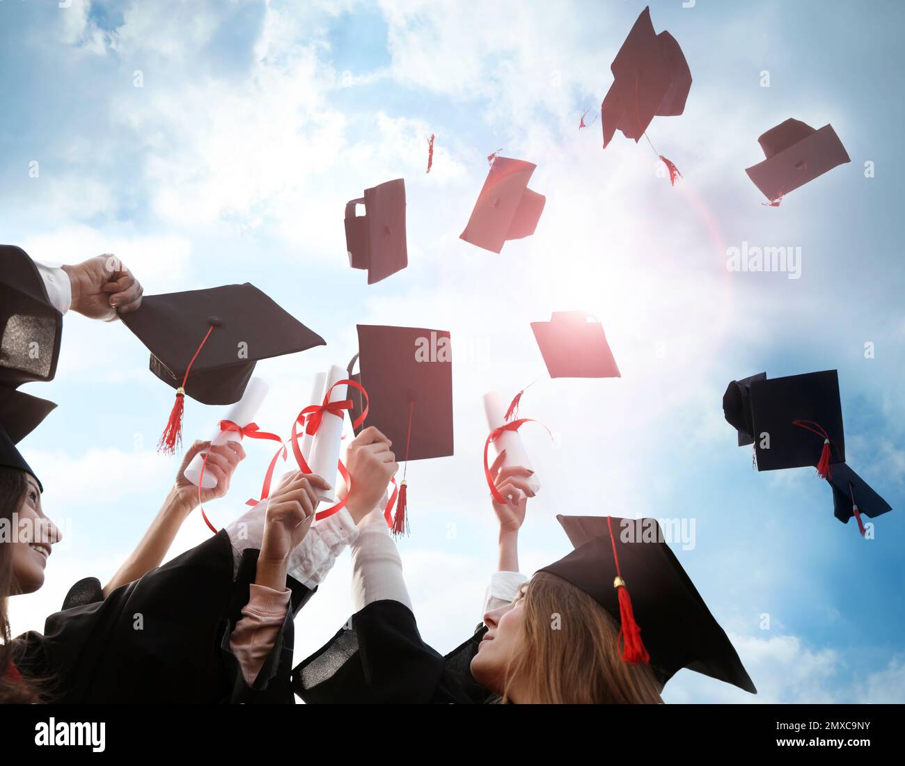 Glückliche Studenten mit Diplomen, die ihre Abschlussmützen draußen in die Luft werfen Stockfoto