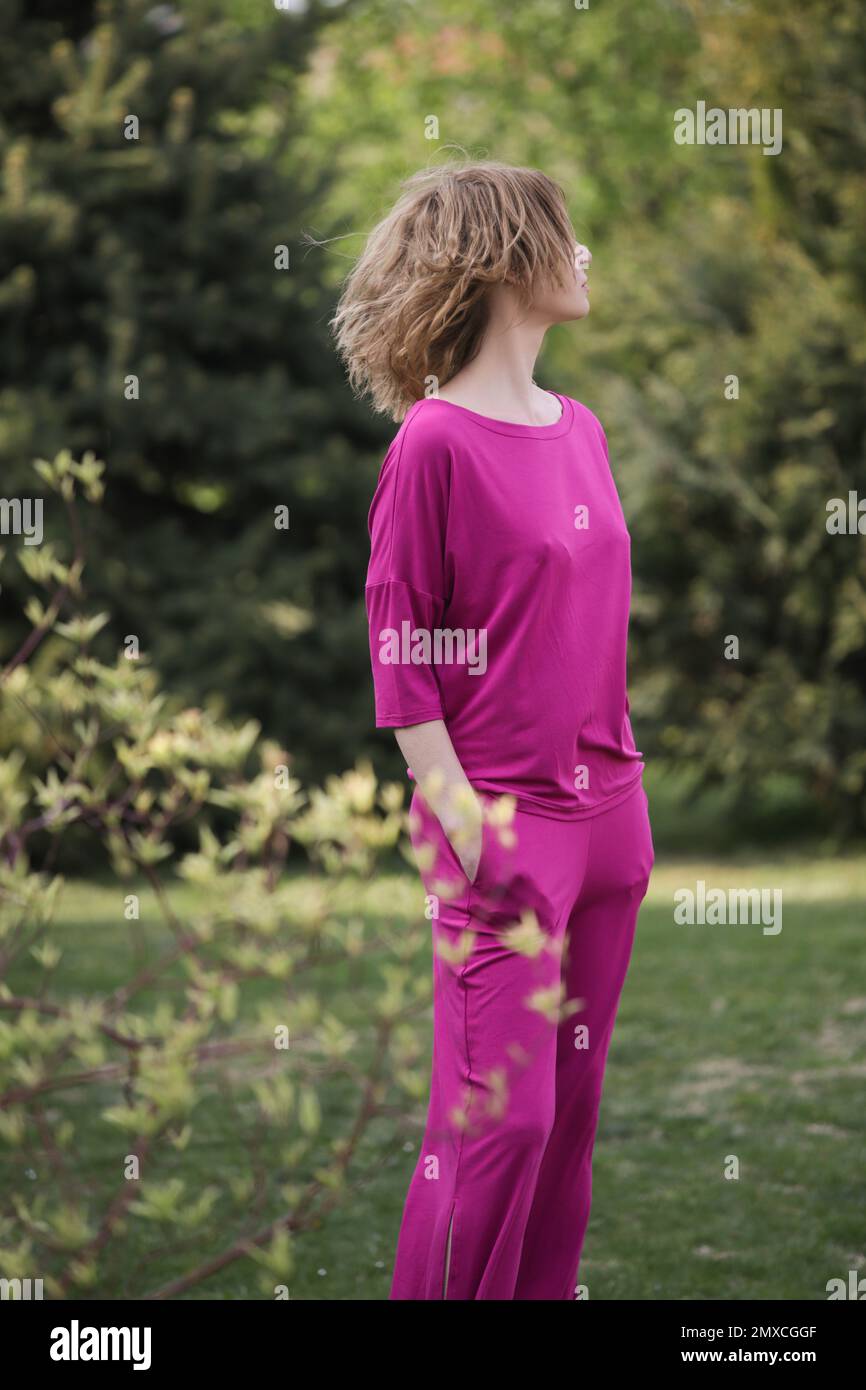 Außenporträt eines weiblichen Models in leuchtend pinkfarbenem Outfit, das an einem wunderschönen Sommertag in der Natur geniesst Stockfoto