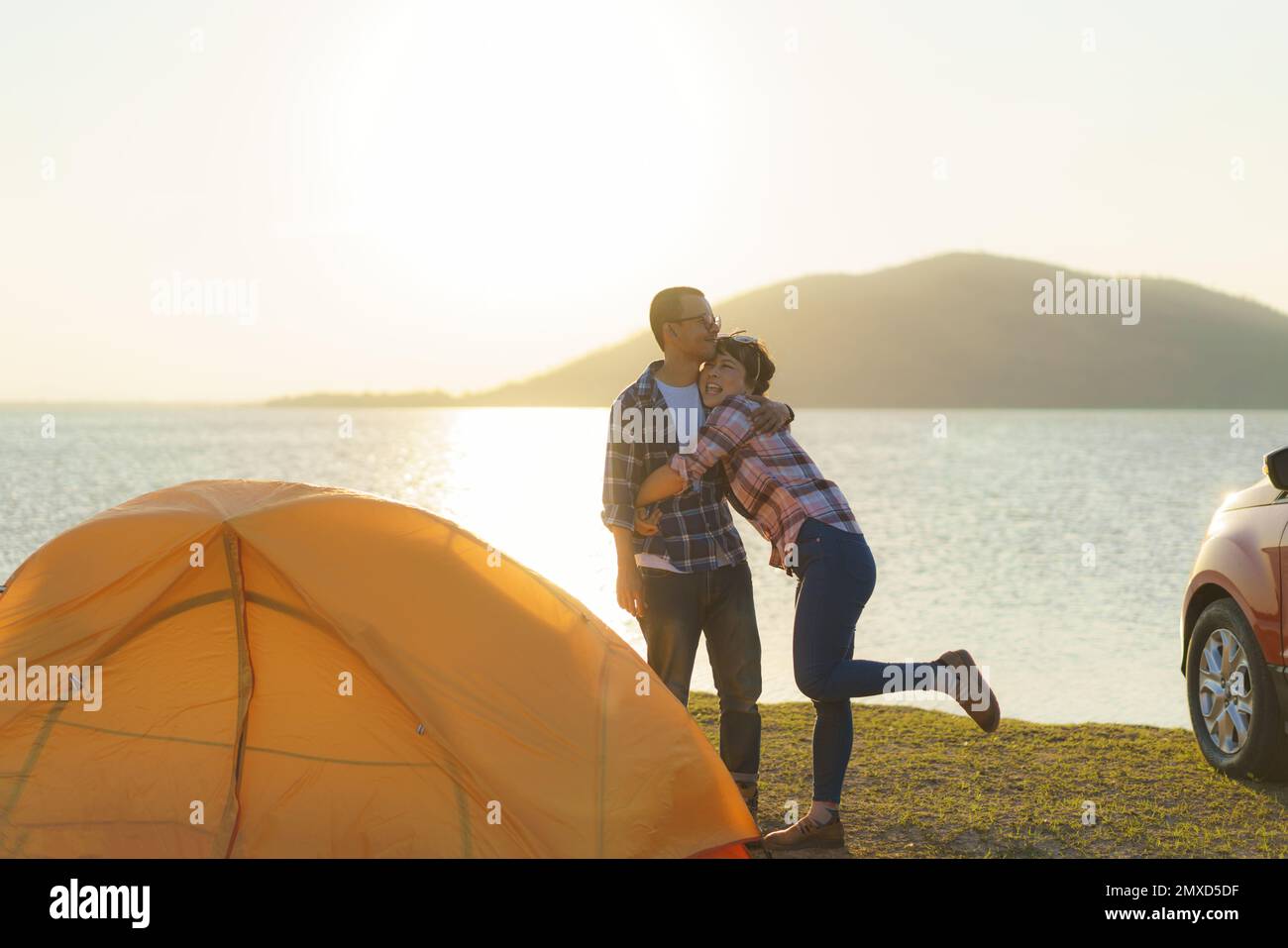 Asiatische Frau, die ihren Freund umarmt, nachdem sie ein Zelt zur Vorbereitung auf das Camping geworfen hat Stockfoto