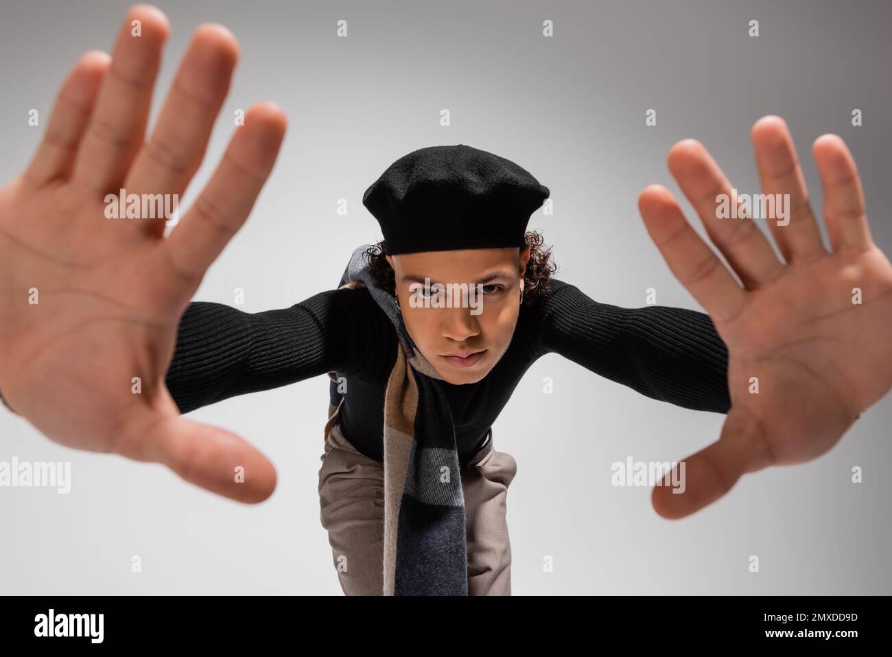 ein afroamerikanischer Mann in trendigen Baskenmützen und schwarzem Pullover, der mit erhobenen Händen auf grauem Hintergrund steht, Stockbild Stockfoto