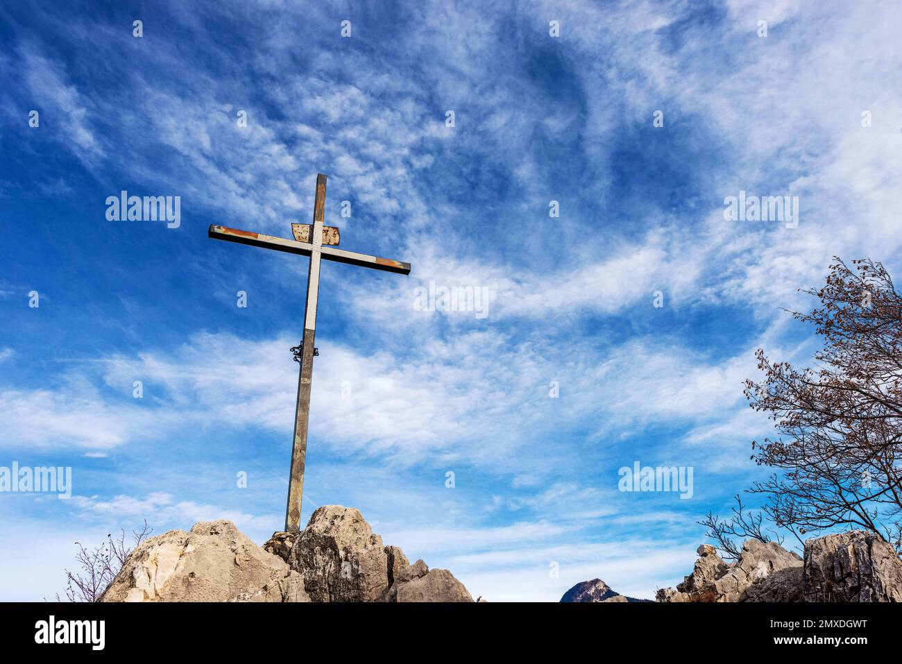 Religiöses Kreuz aus Metall auf einem Berggipfel vor einem blauen Himmel mit Wolken und Kopierraum. Monte Altissimo di Nago, Trentino Alto Adige, Italien Stockfoto