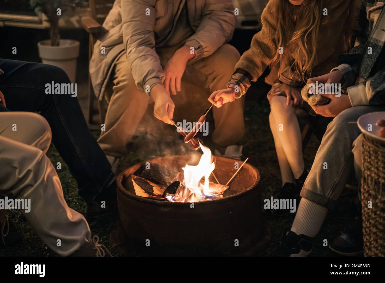 Familienanhänger. Kinder, Bruder Schwester, mom, Dad, Braten Würstchen auf Feuer, essen Hot Dogs. Abendliches Picknick in der Natur. Holiday Barbecue BBQ Food. Urlaub Stockfoto