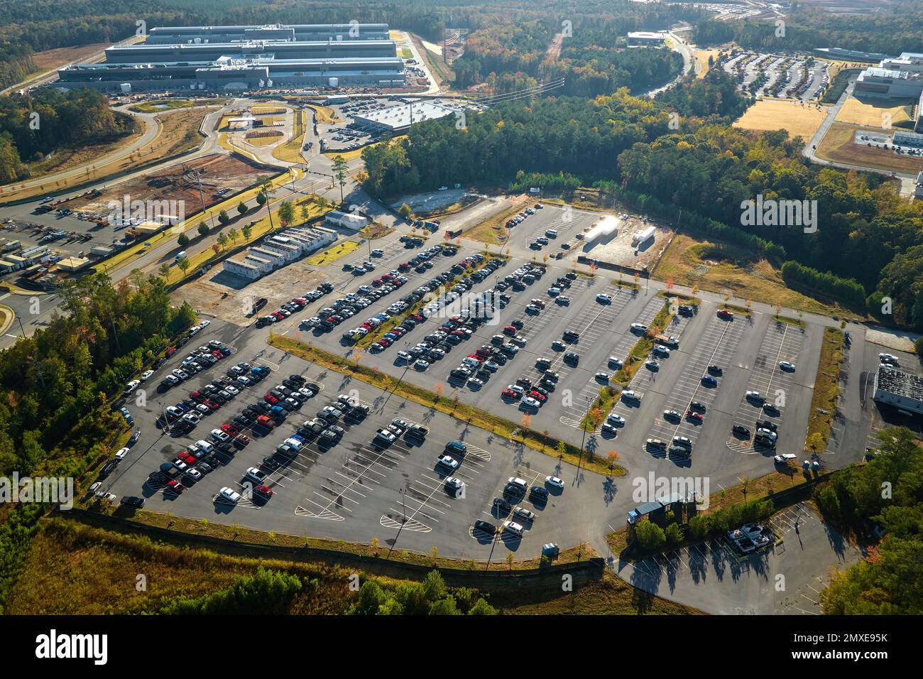 Viele Nebenfahrzeuge parken auf einem großen Parkplatz vor dem Industriewerkgebäude. Fertigung und globales Industriekonzept. Stockfoto