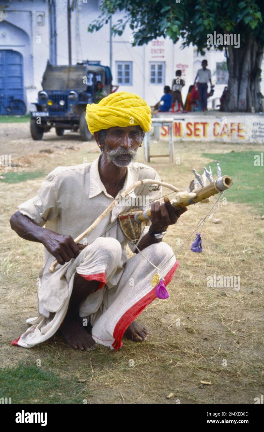 Historisches Archivbild eines Rajashtani-Straßenmusikers in farbenfrohem Turban-Squatting, der ein antikes, gebogenes Folk Instrument oder Ravanahatha spielt, Vorfahren der Violin in Pushkar India 1990 Stockfoto