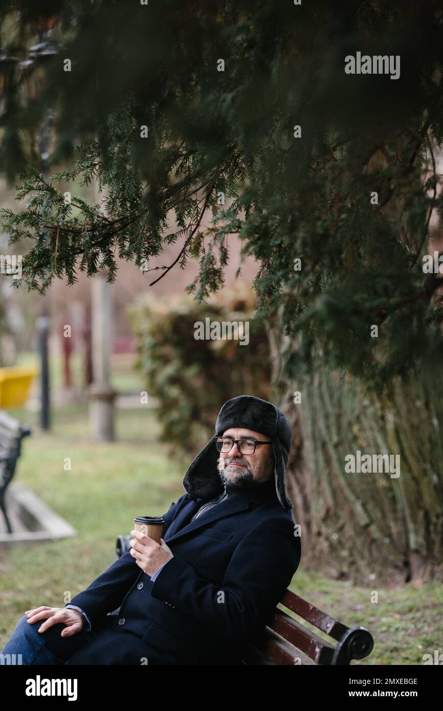 Ein älterer Mann genießt einen kalten Wintermorgen in der Stadt. Ein Mann sitzt auf einer Bank auf dem Platz, das Konzept von Frieden und Vitalität. Stockfoto