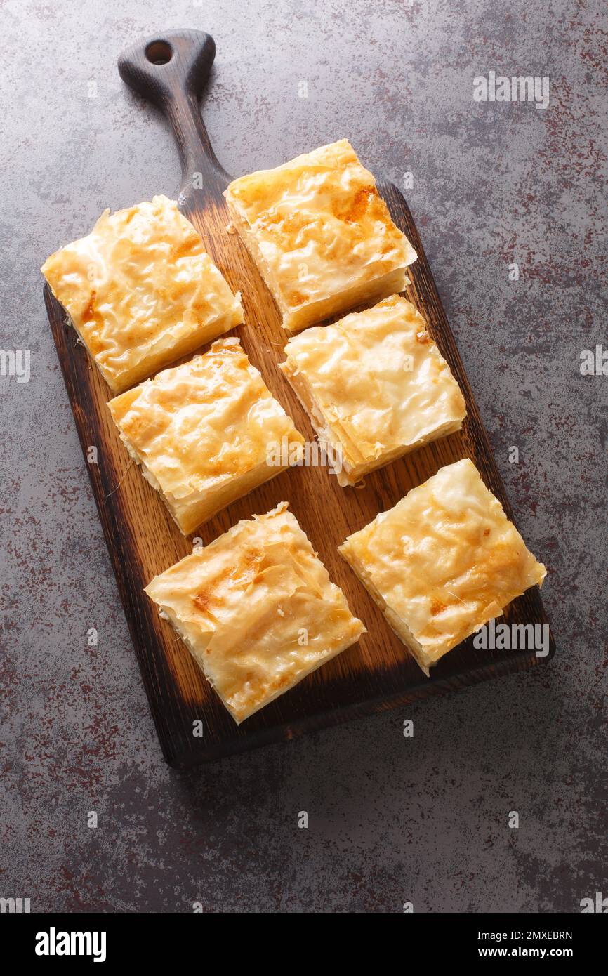Galaktoboureko ist ein traditionelles griechisches Dessert mit einem Vanillesauce in knusprigem Phyllo-Gebäck auf dem Holzbrett auf dem Tisch. Vertikale Draufsicht Stockfoto