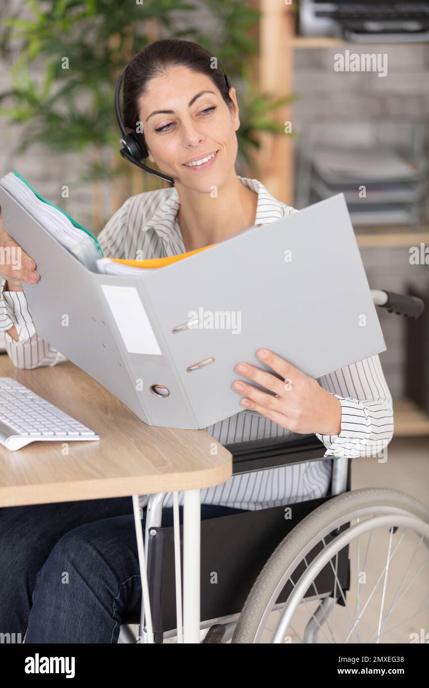 Frau im Rollstuhl, die ein Headset trägt und in der Mappe nachsieht Stockfoto