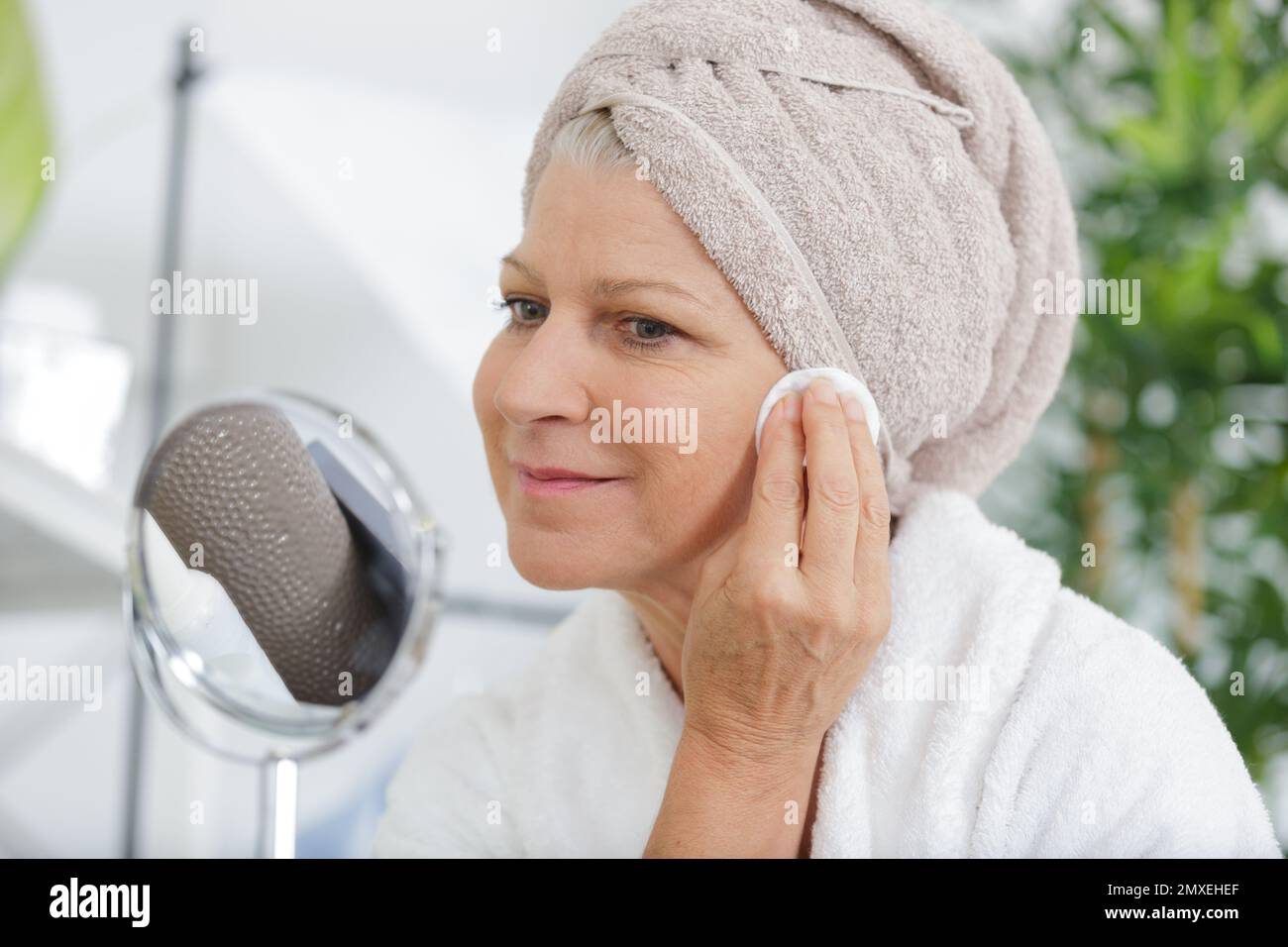 Reife Frau, die im Bad Feuchtigkeitscreme auf ihr Gesicht aufträgt Stockfoto