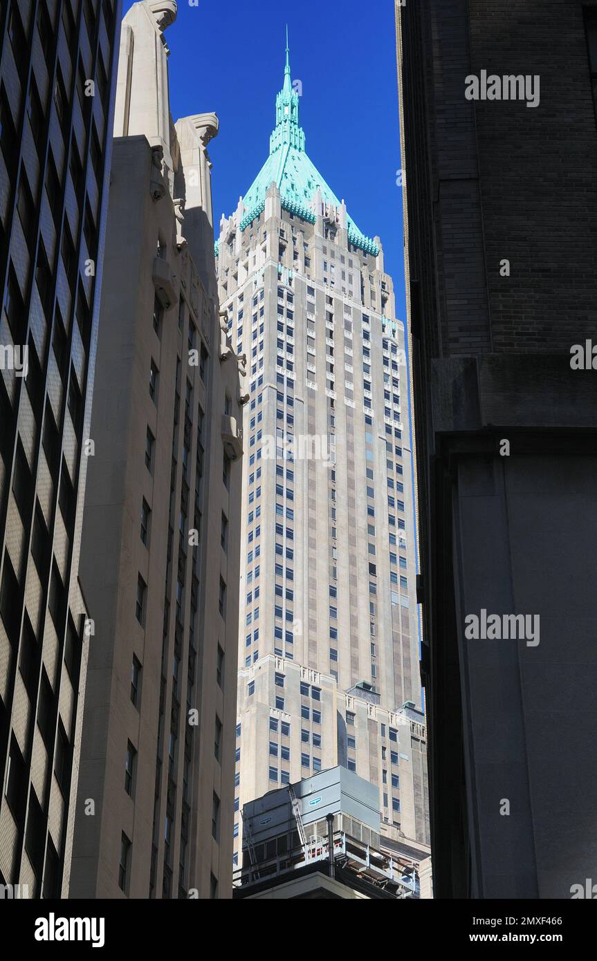 Ein markanter Art déco-Wolkenkratzer mit türkisfarbenem Turm erhebt sich vor einem leuchtend blauen Himmel und zeigt Manhattans legendäre Skyline und historische Architektur Stockfoto