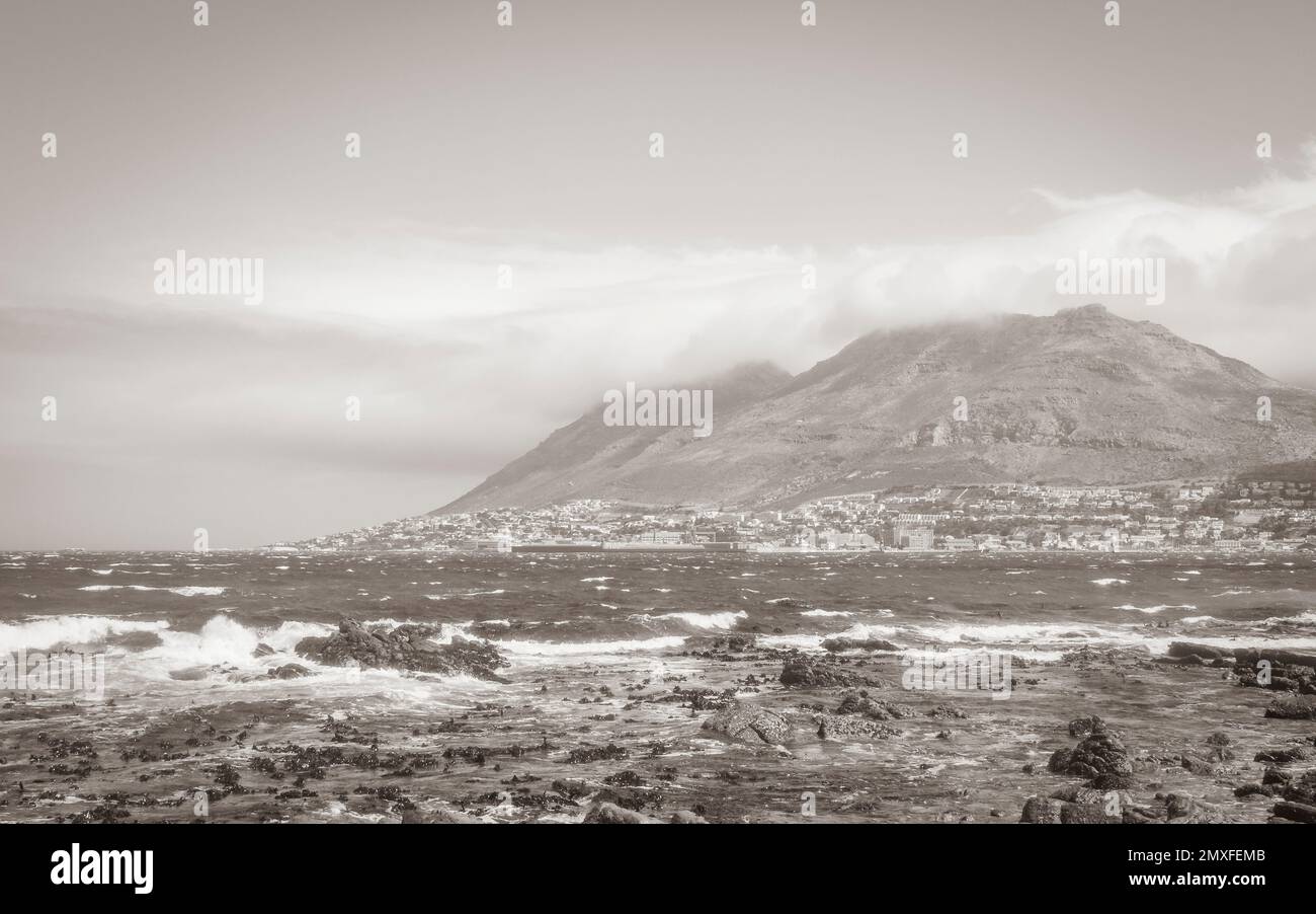 False Bay raue Küstenlandschaft mit Felsbrocken Wellen und Berge mit Wolken in Glencairn Simons Town Kapstadt Westkap Südafrika. Stockfoto