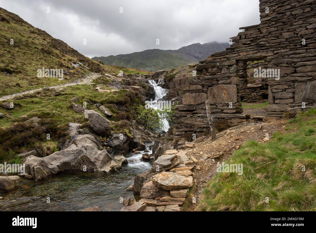 Alte Steinruinen am Fluss auf dem Watkin Path in Cwm Llan. Auf dieser beliebten Route zum Mount Snowdon im Snowdonia-Nationalpark, Wales, sehen viele Besucher. Stockfoto