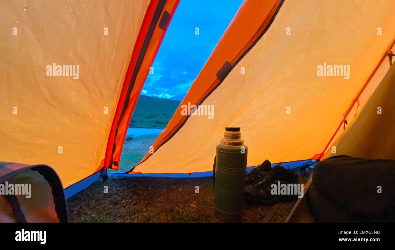 Thermos und Wanderschuhe stehen an einem regnerischen Abend im Altai-Gebirge am offenen Ausgang aus dem Zelt Stockfoto