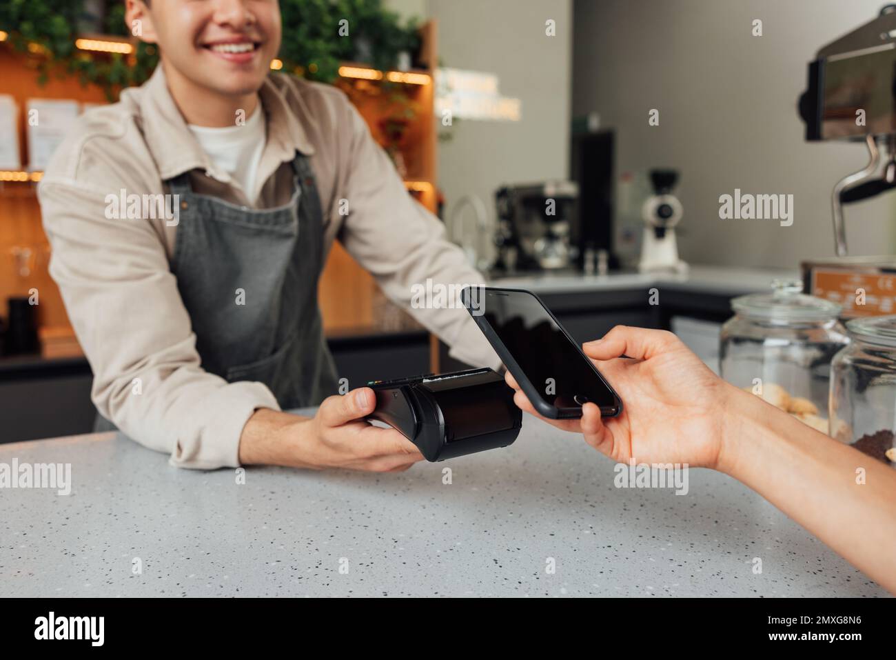 Nicht wiederzuerkennen, dass der Besitzer des Cafés den Kartenautomaten am Tresen hält, während der Gast die Zahlung per Smartphone tätigt Stockfoto