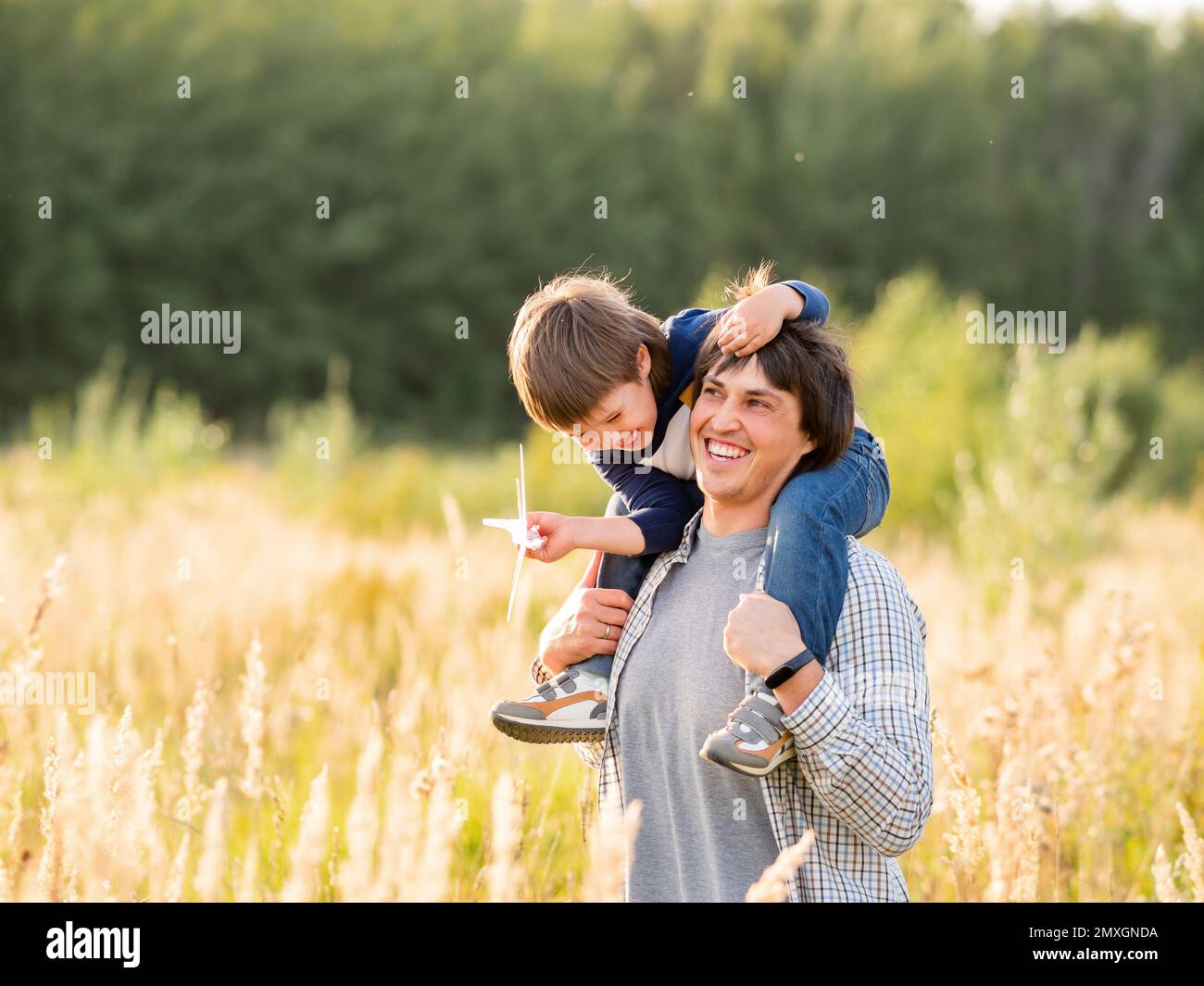 Niedlicher Junge und sein Vater spielen mit Spielzeug Flugzeug. Glückliches Kind träumt davon, Pilot zu sein. Boy plant für die Zukunft. Vater und Sohn auf dem Feld bei goldenem Sonnenuntergang Stockfoto