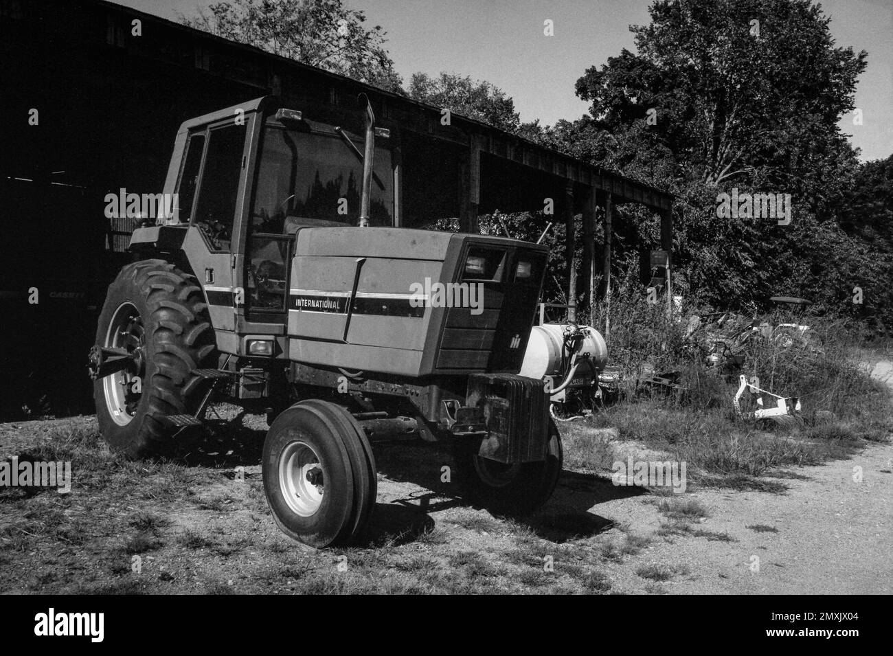 Ein moderner internationaler Traktor, der vor einer Scheune im Gras auf einem Bauernhof geparkt ist. Littleton Massachusetts. Das Bild wurde in analogem Schwarzweiß aufgenommen Stockfoto