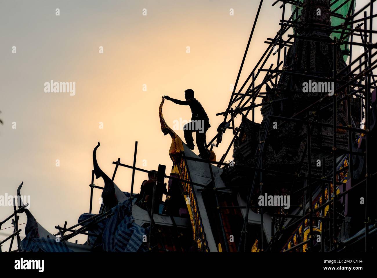 Wat Yannawa, Bangkok, Thailand, 18. Januar 2023: Silhouette der Bauarbeiter auf einem Tempeldach, der goldene Giebelspitzen repariert. Stockfoto