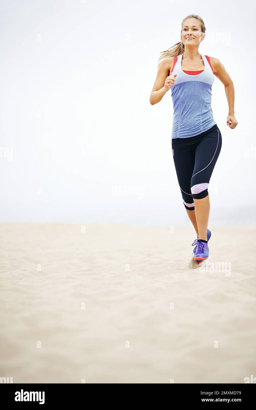 Werde bei jedem Schritt fitter. Eine junge Frau, die am Strand joggt. Stockfoto