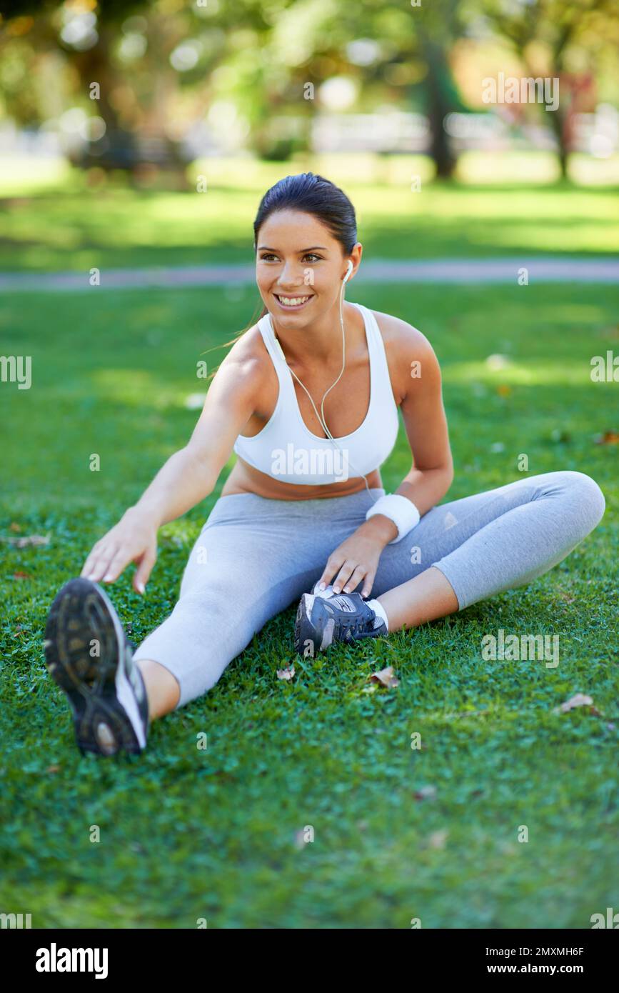 Sie weiß, wie wichtig Dehnübungen sind. Eine wunderschöne junge Frau, die sich im Park streckt. Stockfoto