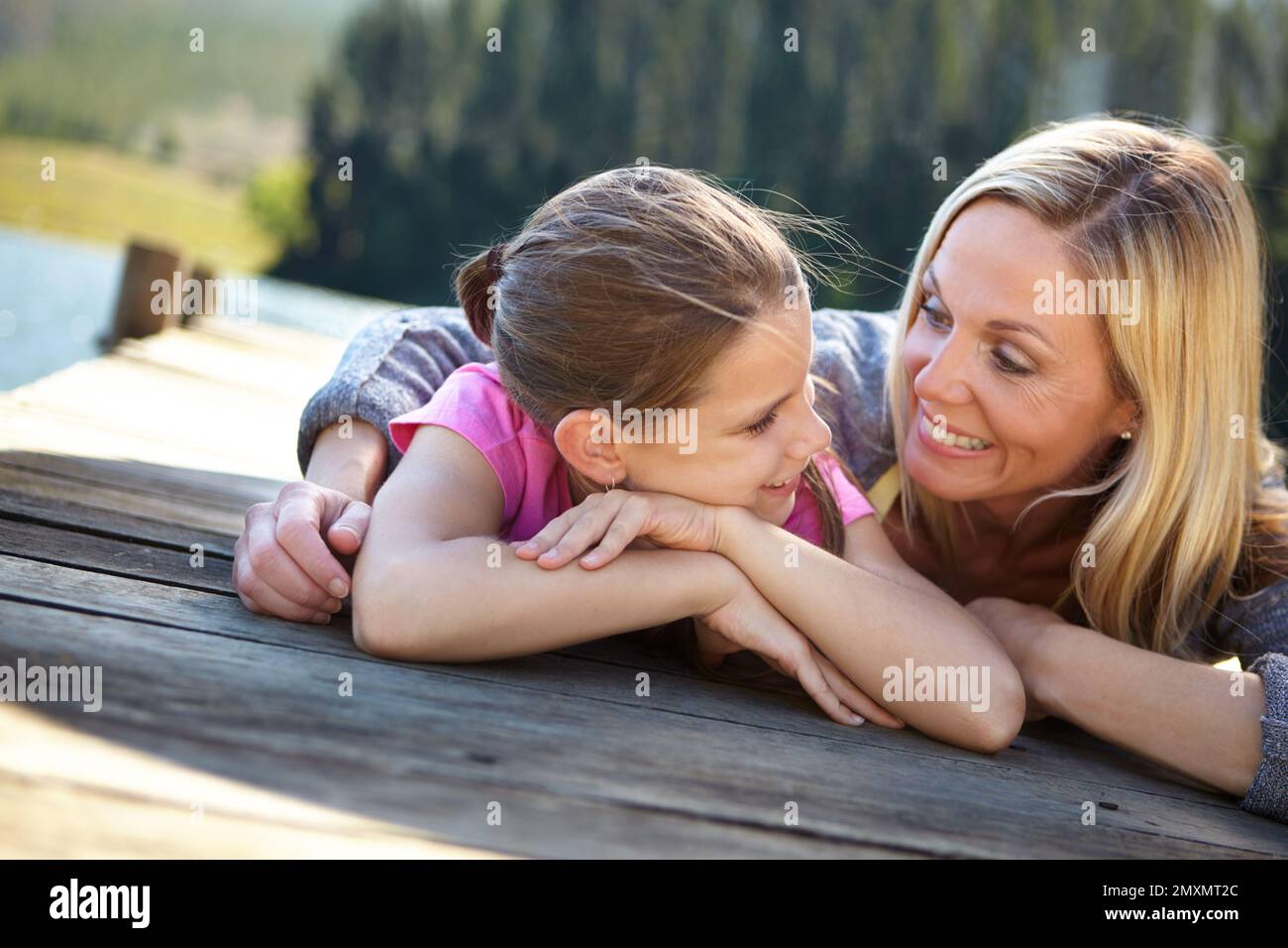 Sie kichert über Frauengespräche. Eine Mutter und eine Tochter, die auf einem Pier an einem See liegen. Stockfoto