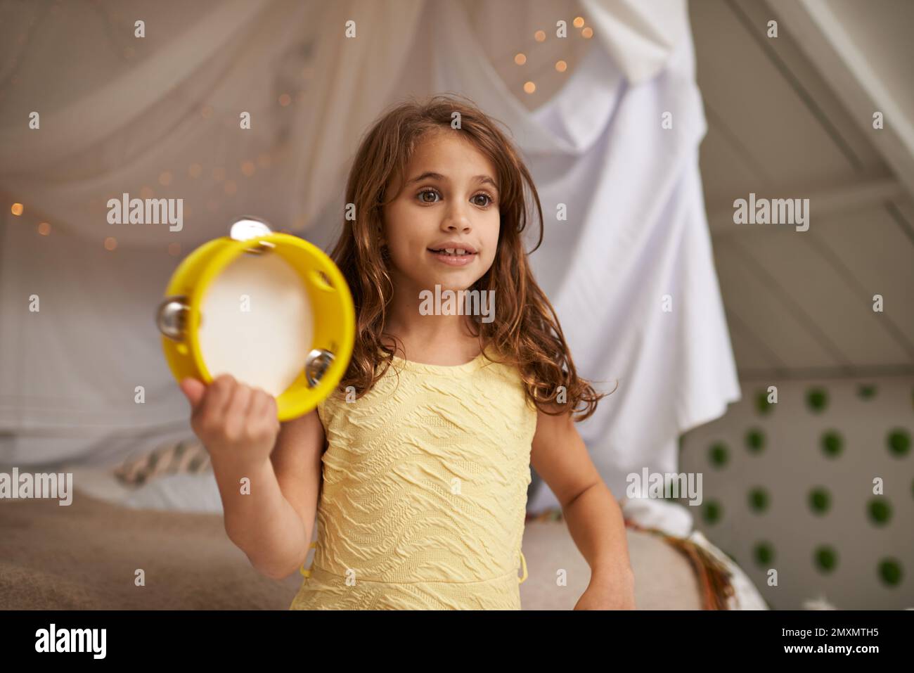 Sie ist ein Tamburin-Mädchen. Ein süßes kleines Mädchen, das drinnen mit Tamburin spielt. Stockfoto