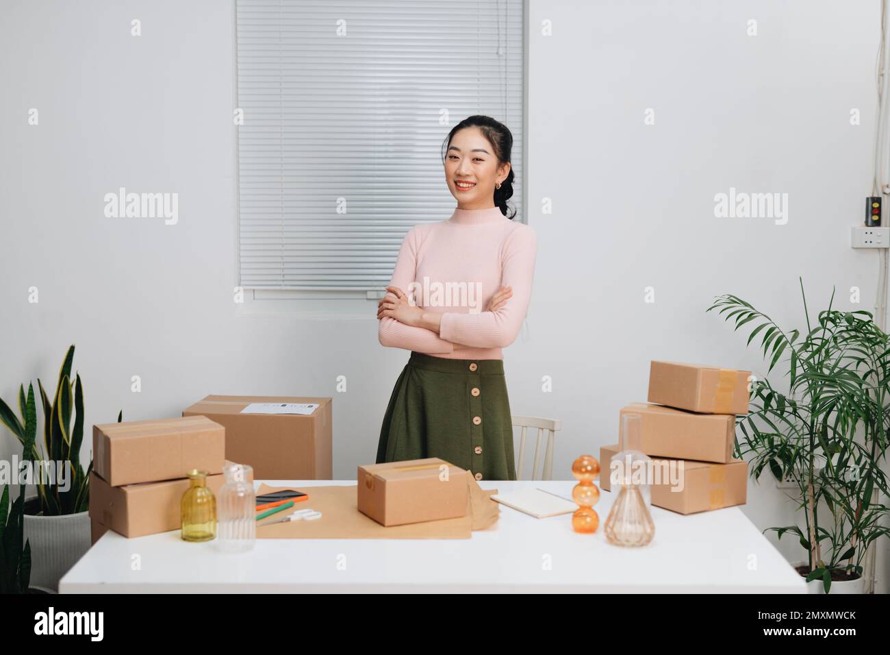 Weibliche Inhaberin eines kleinen Unternehmens, die mit gekreuzten Armen steht und vor der Kamera lächelt. Stockfoto