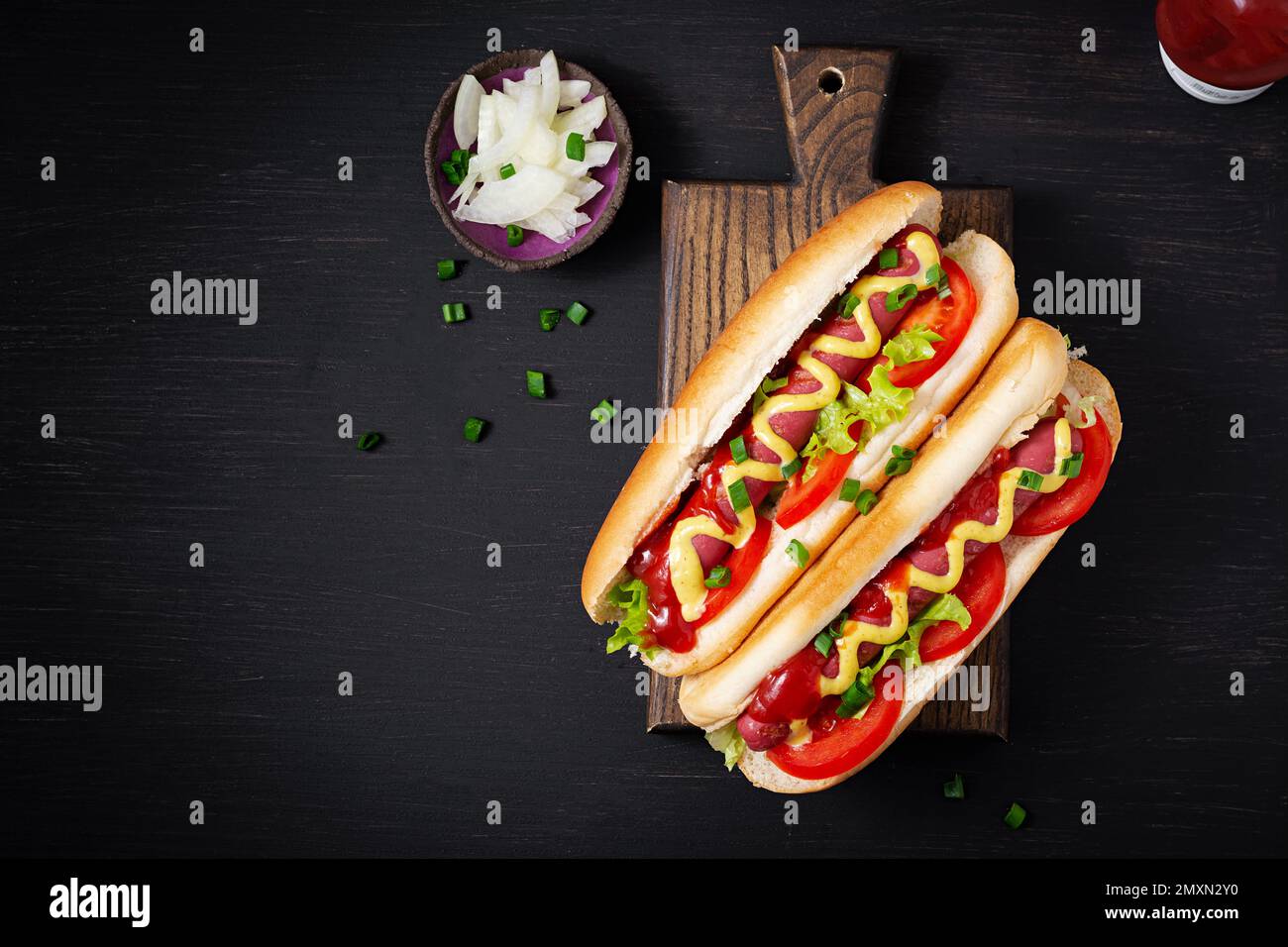 Hot Dog mit gegrillter Wurst, Tomaten und Salat auf dunklem Hintergrund. Amerikanischer Hotdog. Draufsicht, über Kopf Stockfoto