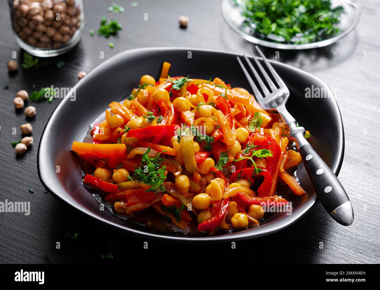 Gemüseeintopf aus Kichererbsen, Karotten, Gemüsepaprika, Zwiebeln, Knoblauch und Tomatensoße mit Zitrone auf dem dunklen Tisch. Orientalische Küche. Stockfoto