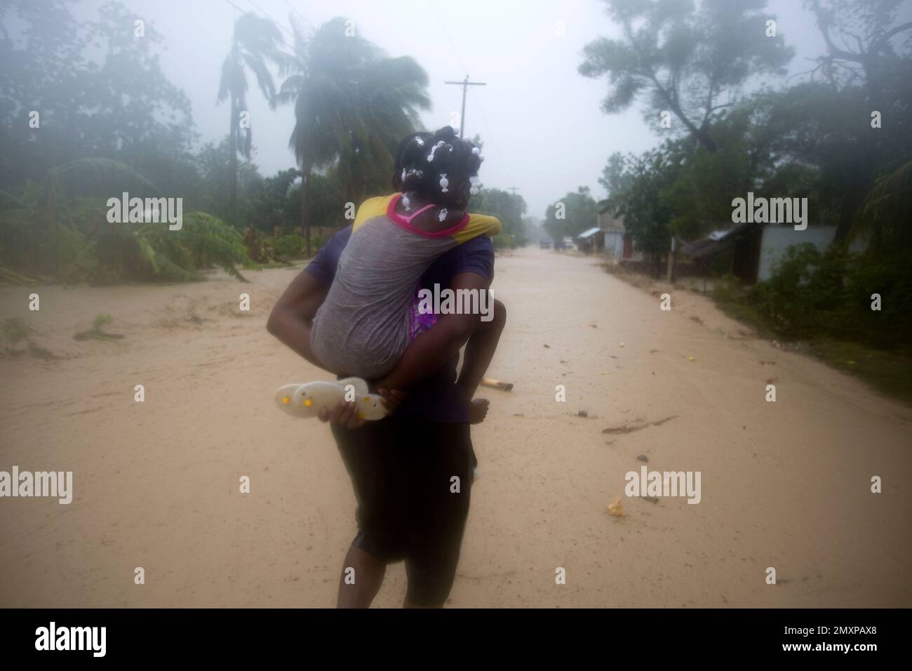 A woman carries a child through a waterlogged street as they head to a