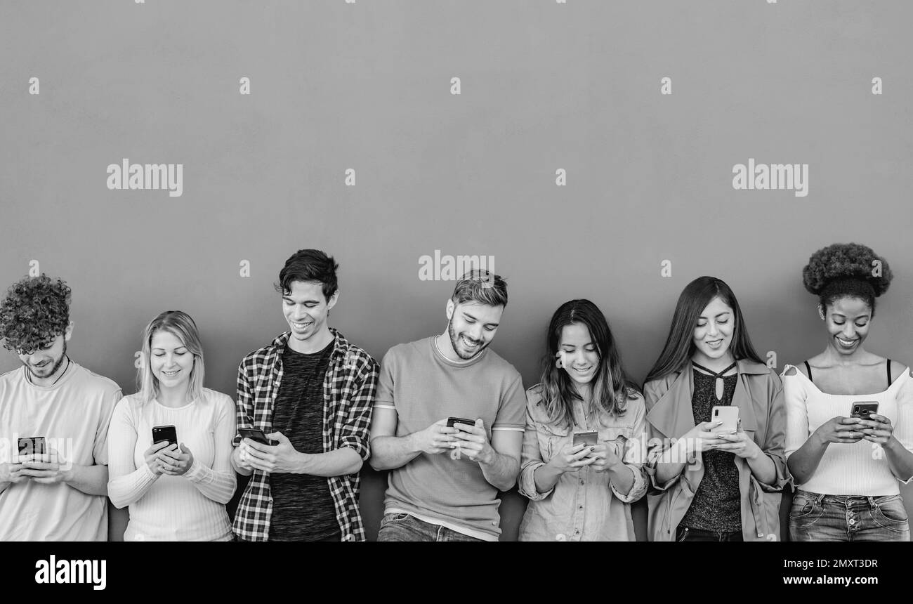Junge, multiethnische Gruppe von Freunden, die ihr Smartphone im Freien nutzen – Konzept der Jugend- und Technologieabhängigkeit – Schwarzweiß-Bearbeitung Stockfoto