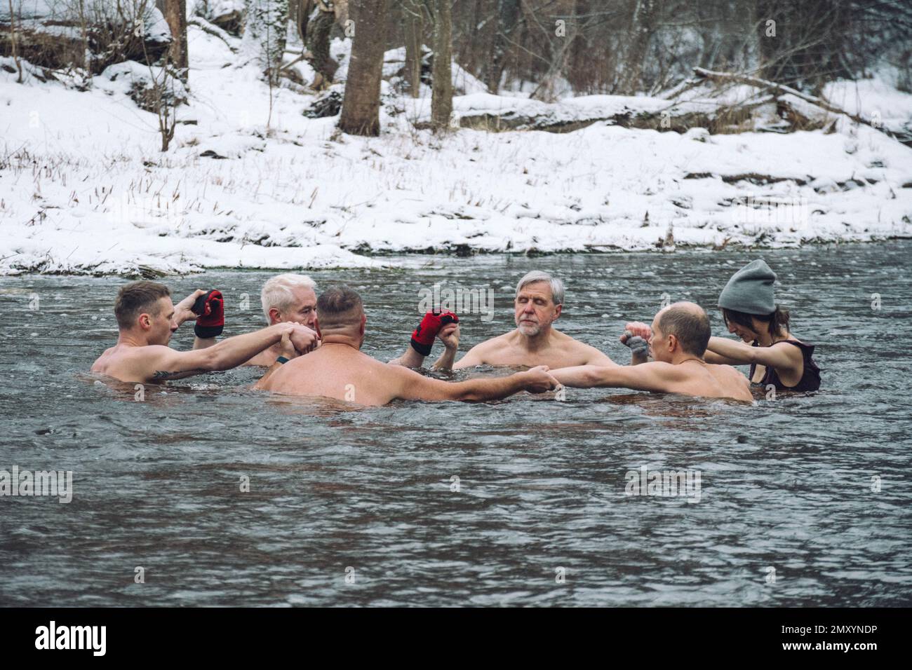 Gruppe von Personen im Kreis, die gemeinsam im kalten Wasser eines Flusses in einem Wald baden. Wim Hof Methode, Kältetherapie, Atemtechniken, Yoga Stockfoto