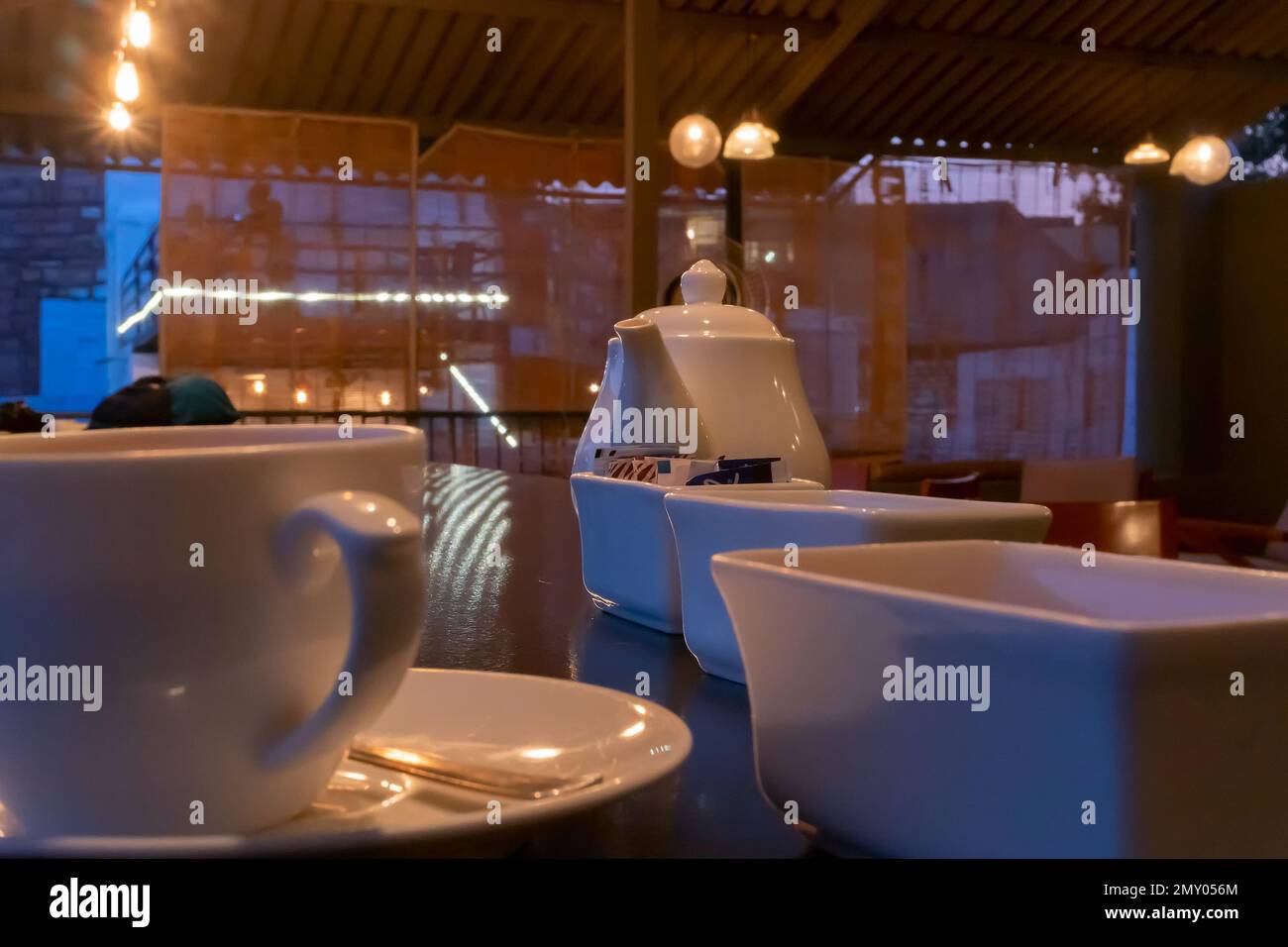 Wunderschöner Blick auf das Restaurant im Jodhpur Rajasthan, Indien. Weiße Tassen, Geschirr und Teekanne mit Reflektoren von dekorierten Lichtern auf dem glänzenden Tisch Stockfoto