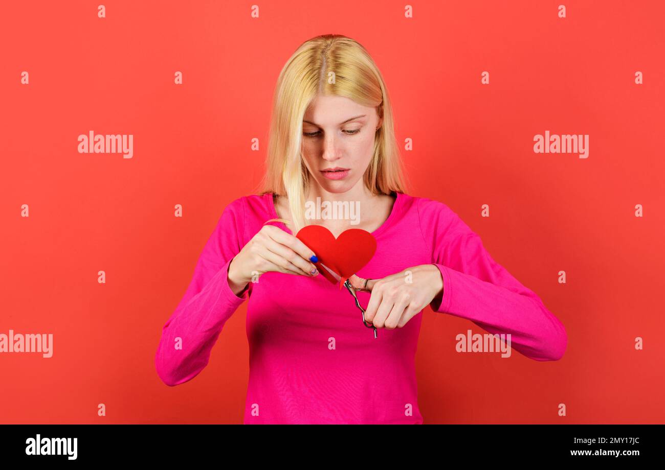 Trauriges Mädchen schneidet rotes Herz mit einer Schere. Paare divergieren. Beziehungen brechen, Streit und Scheidung. Stockfoto