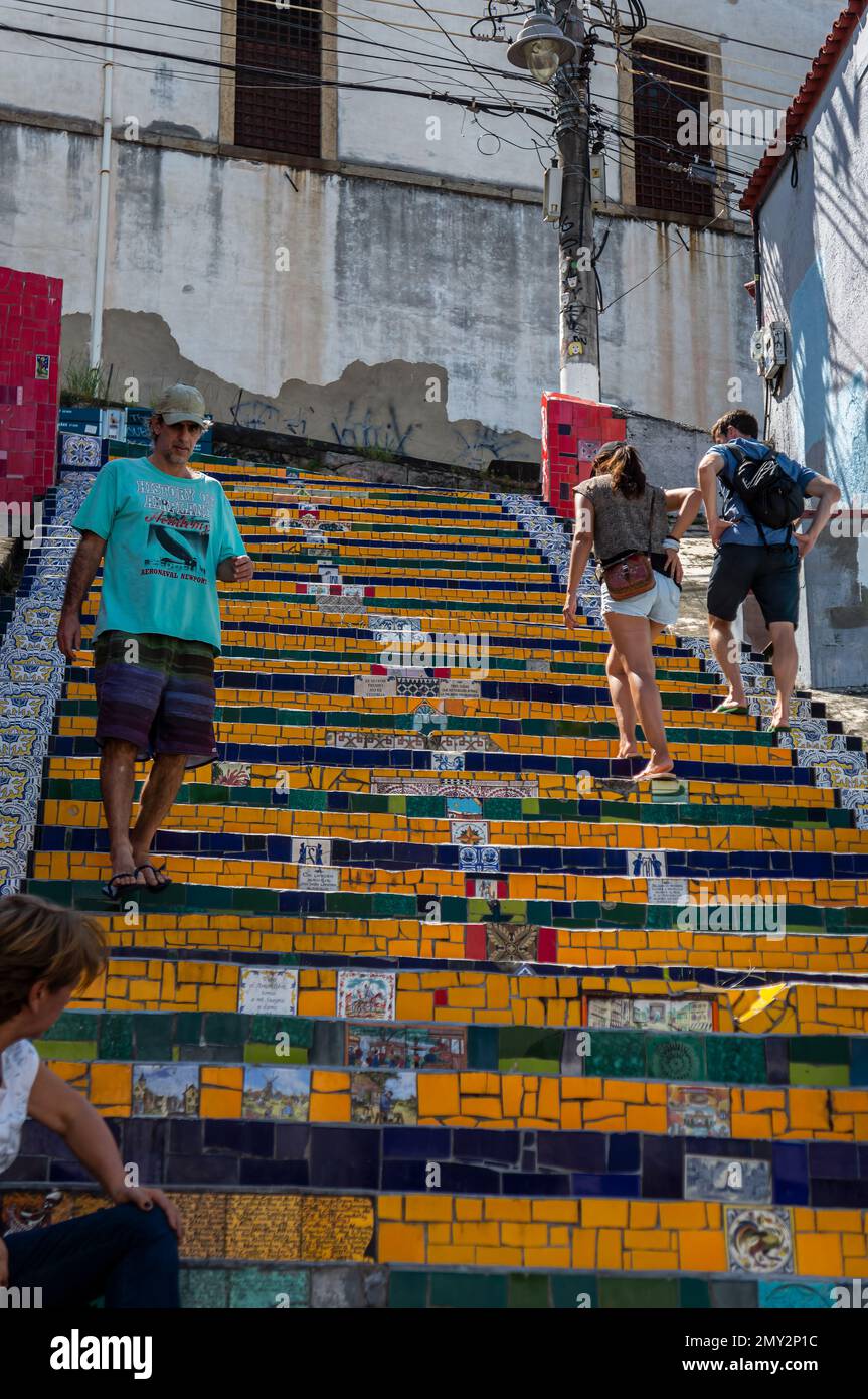 Touristen, die an einem sonnigen Sommertag an den farbenfrohen Keramikfliesen der Selaron Treppe im Viertel Santa Teresa in der Nähe der Ladeira de Santa Teresa Straße vorbeilaufen. Stockfoto