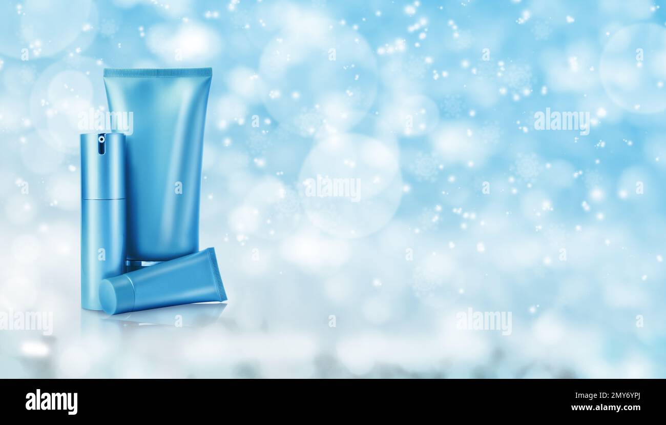 Verschiedene kosmetische Mittel auf hellblauem Hintergrund mit verschwommenen Schneeflocken, Platz für Text. Winterhautpflege Stockfoto