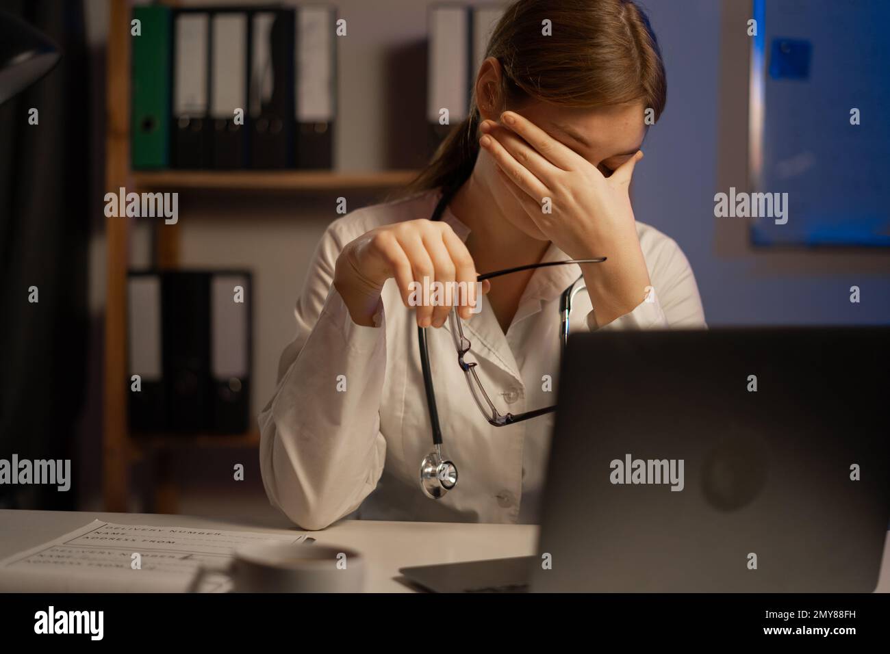 Müder Arzt oder Krankenpfleger, der während der Nachtschicht am Tisch sitzt. Speicherplatz kopieren Stockfoto