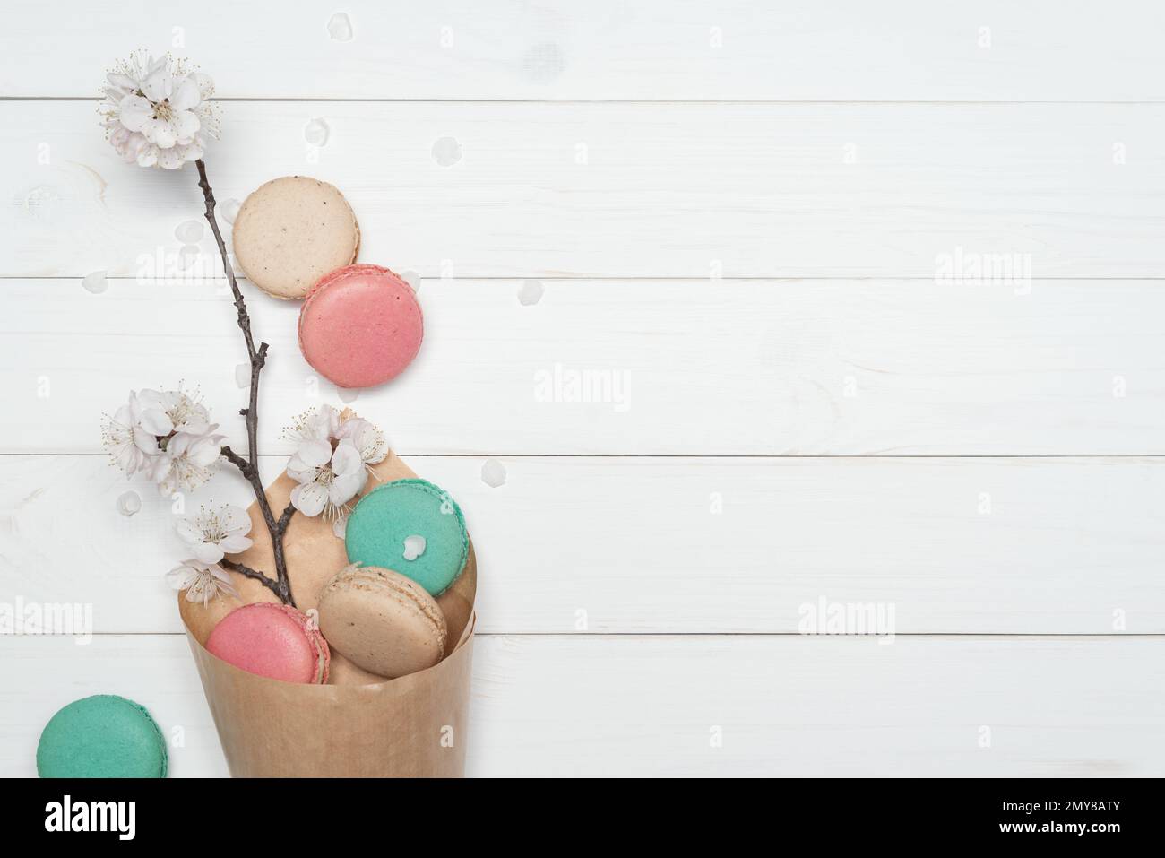 Papiertüten mit Keksen, Makronen in verschiedenen Farben. Köstliches französisches Dessert auf weißem Holzhintergrund. Ast mit den Blumen des Aprikosenbaums. Te Stockfoto