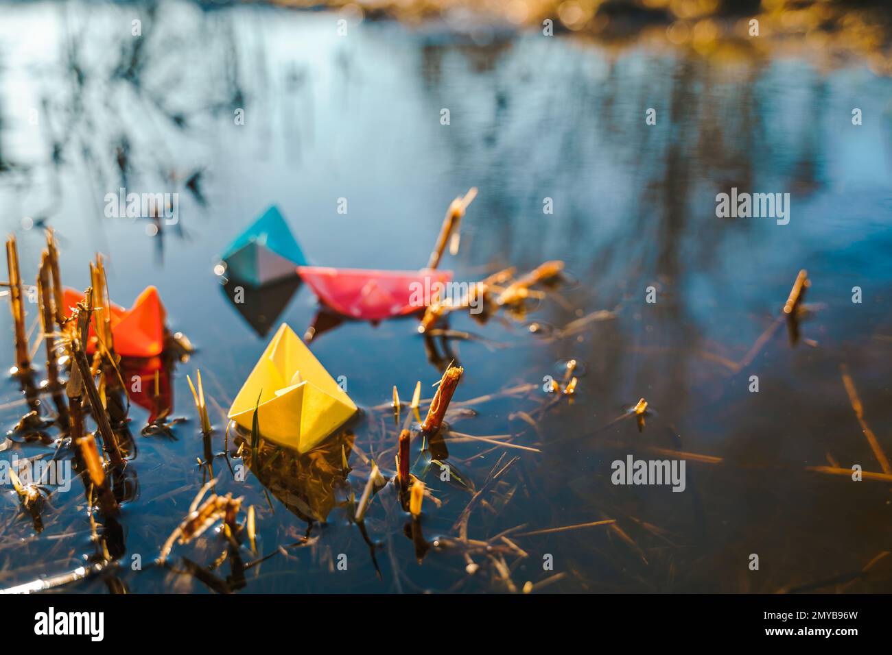 Mehrfarbige Papierboote. Farbenfrohe rosafarbene, blau-orange Schiffe in einer großen Schneepfütze im Frühling auf der Winterstraße. Warmes, nasses Regenwetter, altes Gras. Hallo Stockfoto