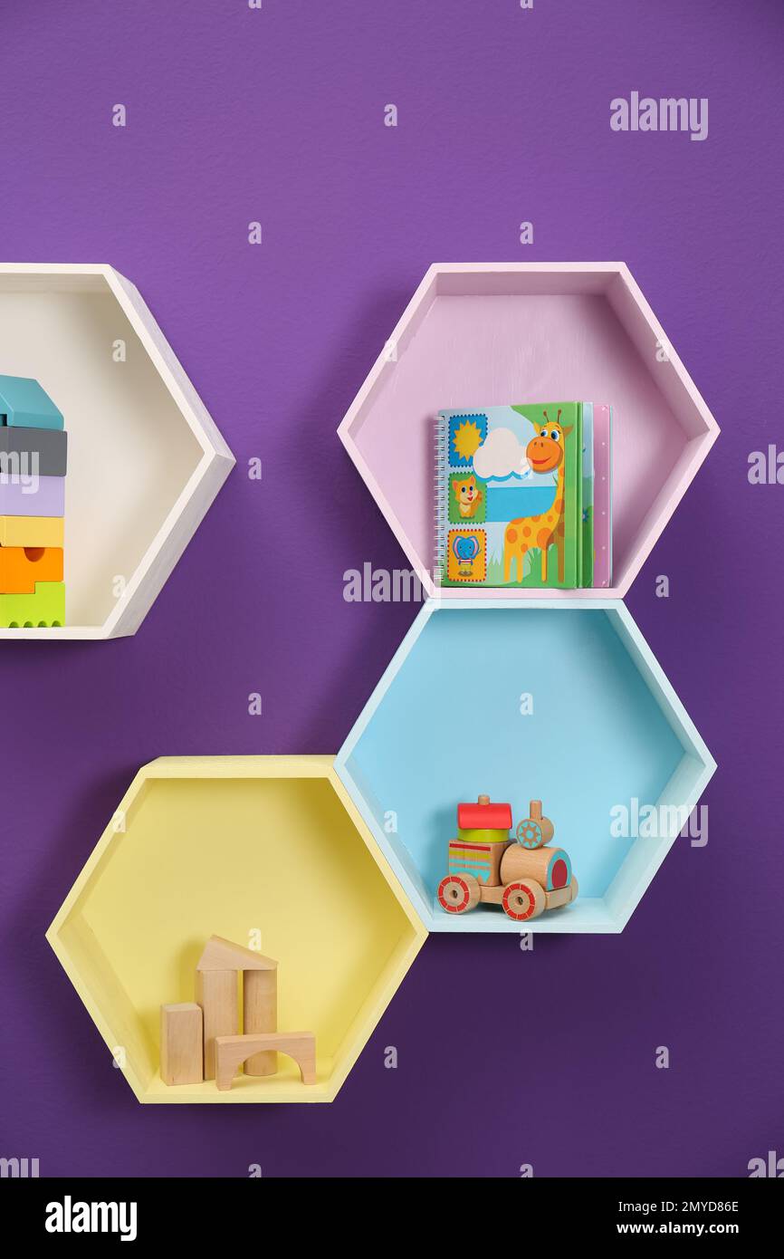 Sechseckige Regale mit Spielzeug an lila Wänden. Innendesign Stockfoto