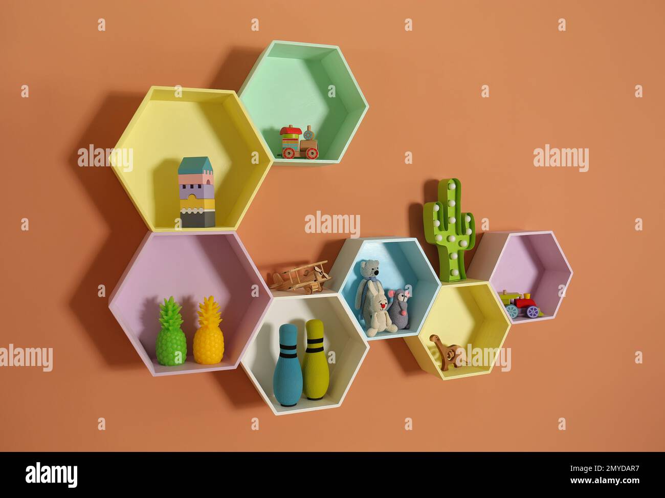 Sechseckige Regale mit Spielzeug an orangefarbenen Wänden. Innendesign Stockfoto